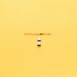Minimalist image of a syringe and vaccine vial on a vibrant yellow background.