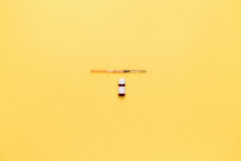 Minimalist image of a syringe and vaccine vial on a vibrant yellow background.
