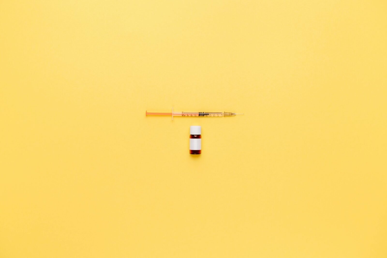 Minimalist image of a syringe and vaccine vial on a vibrant yellow background.