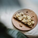 Sliced banana and peanut butter on rye toast presented on a wooden plate, offering a healthy snack.